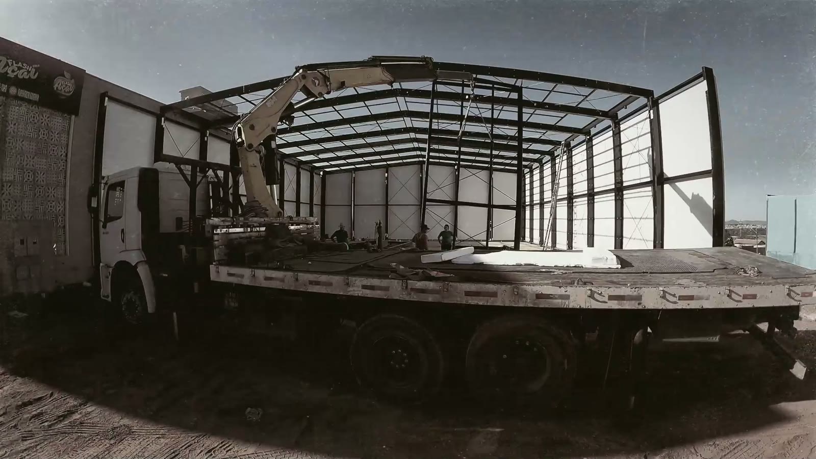 Caminhão com painéis chegando à obra ao lado da estrutura montada